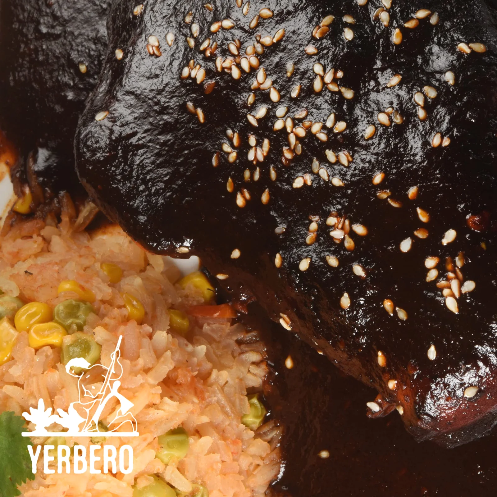 Close view of a chicken leg coated in glossy dark mole with sesame seeds, over rice with corn and peas